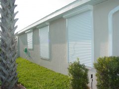 new, white automatic shutters installed on a house in Fort Myers FL. Shutters are in the closed position over the windows.
