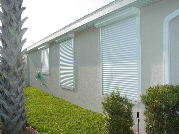 new, white automatic shutters installed on a house in Fort Myers FL. Shutters are in the closed position over the windows.