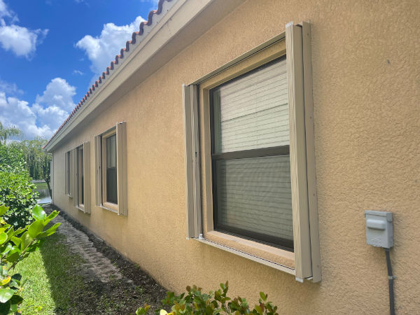 Open, beige accordion shutters shown on four windows of a home in Fort Myers