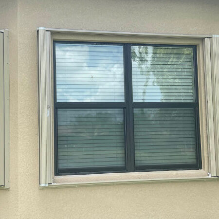 Beige accordion hurricane shutters shown open on a window