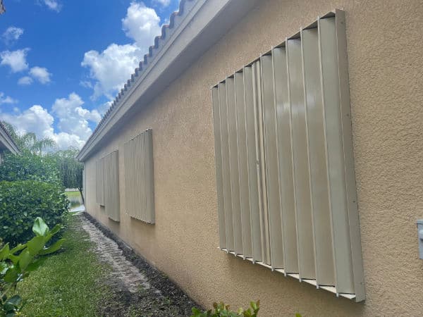 Beige accordion shutters protecting windows of a tan home