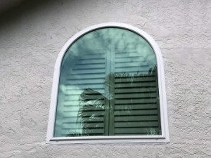 White arch style impact window with tinted glass on a grey stucco home