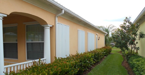 White storm shutters installed on the windows of a yellow home.