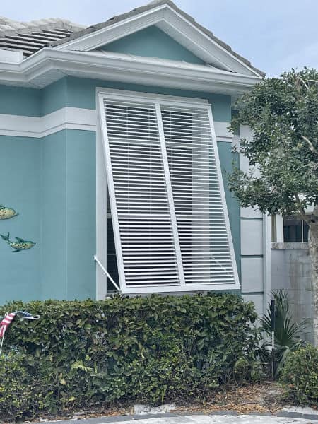 White aluminum Bahama shutter shown on a blue home