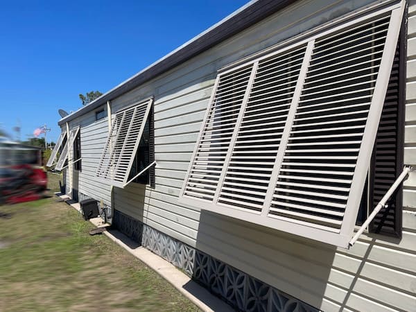 Beige Bahama hurricane shutters on the side windows of a beige modular home in North Fort Myers