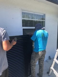 Two Eurex Shutters employees preparing to install a custom black Bahama Shutter on a home in Lehigh Acres FL