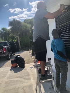 Two members of the Eurex Shutters team installing a custom black Bahama shutter on a home in Lehigh Acres FL