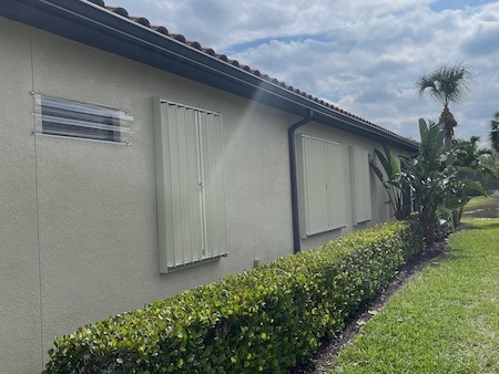 Beige accordion shutters closed over three windows on a beige home in Fort Myers Florida