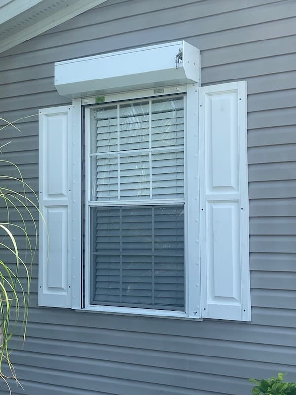 A white Eurex Shutters Rolling Hurricane Shutter installed on a double hung window of a beige manufactured home in South Fort Myers FL