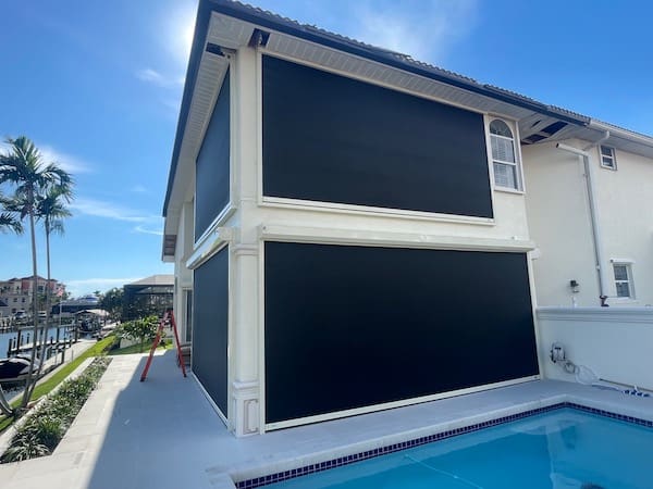 Four manual, hurricane screen systems installed on the ground and second floor of a canal pool home in Cape Coral FL. The kevlar screens are black and the frames and housing boxes are ivory colored.