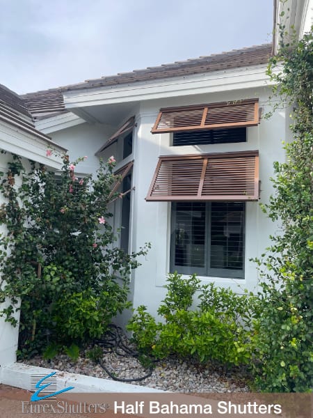 Double decorative bahama shutters installed on multiple windows of an off-white stucco home with a dark brown door in Sanibel FL