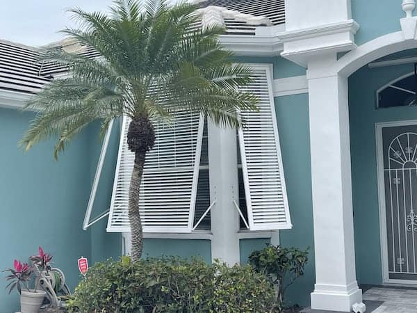 White hurricane shutters installation on a green home in Southwest Florida
