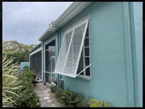 A wide white, full-view, Bahama shutter installed over three windows on the side of a home. In Englewood Florida.