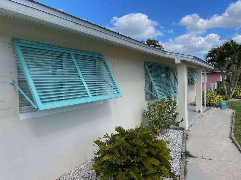 Three custom, blue, full-view, Bahama shutters installed over the front windows of a home. In Lehigh Acres Florida