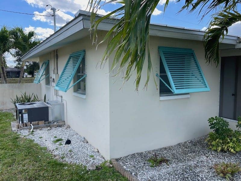 Custom, tiffany blue, Bahama shutters shown installed on the rear and right side of a residential home.