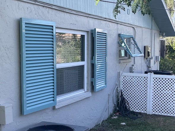 One, custom, tiffany blue, full view Bahama shutter and one custom, tiffany blue colonial shutter, installed over windows on the side of a home. Venice Florida. 