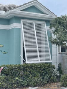 White full-view Bahama shutter covering a single window of a home.