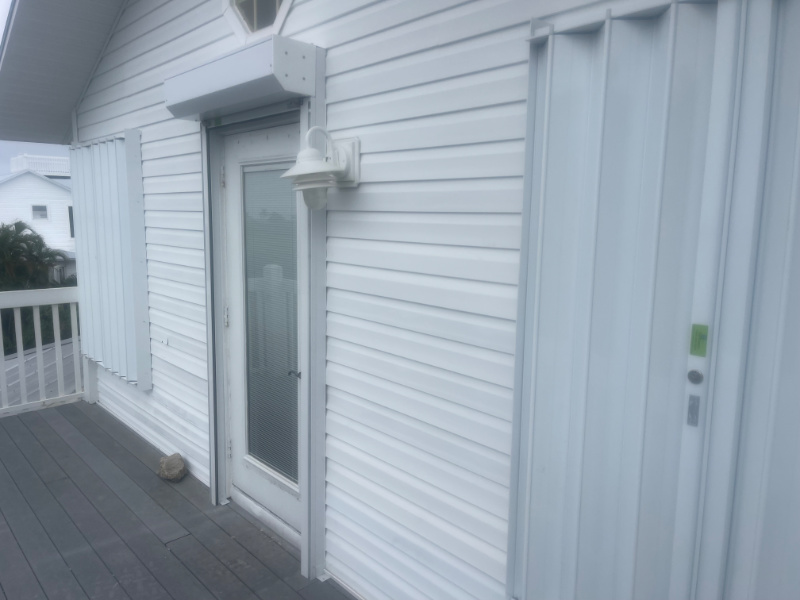 View from the right side of home. White accordion shutters and roll down shutters installed on the doors and windows of a white home in Bokeelia Florida. 