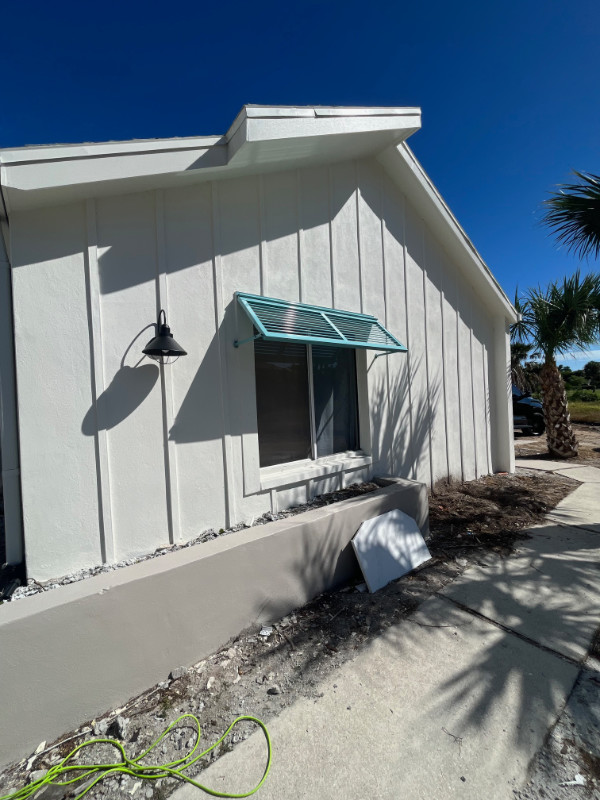 A blue deco half-bahama shutter installed over a window of a white, new construction home on Sanibel.