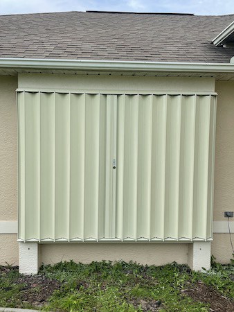 Ivory accordions shown closed over the front window of a tan home.