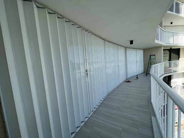 A wide width span of white colored accordion shutters shown closed over the patio doors on a condo in Marco Island Florida.