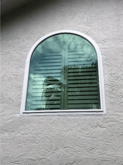 Custom impact window with arch top installed on a beige home.