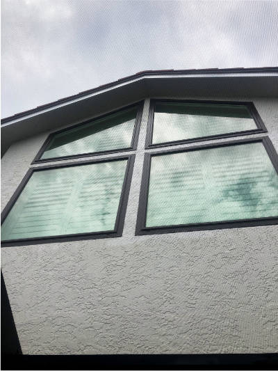 Custom impact windows installed on a beige home in Bonita Springs. Window types include square picture windows, and quadrilateral impact windows