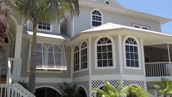 White modern bahama shutters installed on a tan coastal home