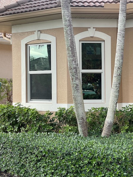 House in Naples, Florida, with a tree in front, showcasing newly installed impact windows by Eurex Shutters.