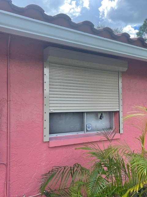 Beige roll shutters shown in a partially open position on a window. Beige slats, beige tracks and beige housing box on a salmon home.